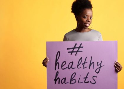Portrait of a woman holding a healthy habits sign, set against a vibrant yellow background.