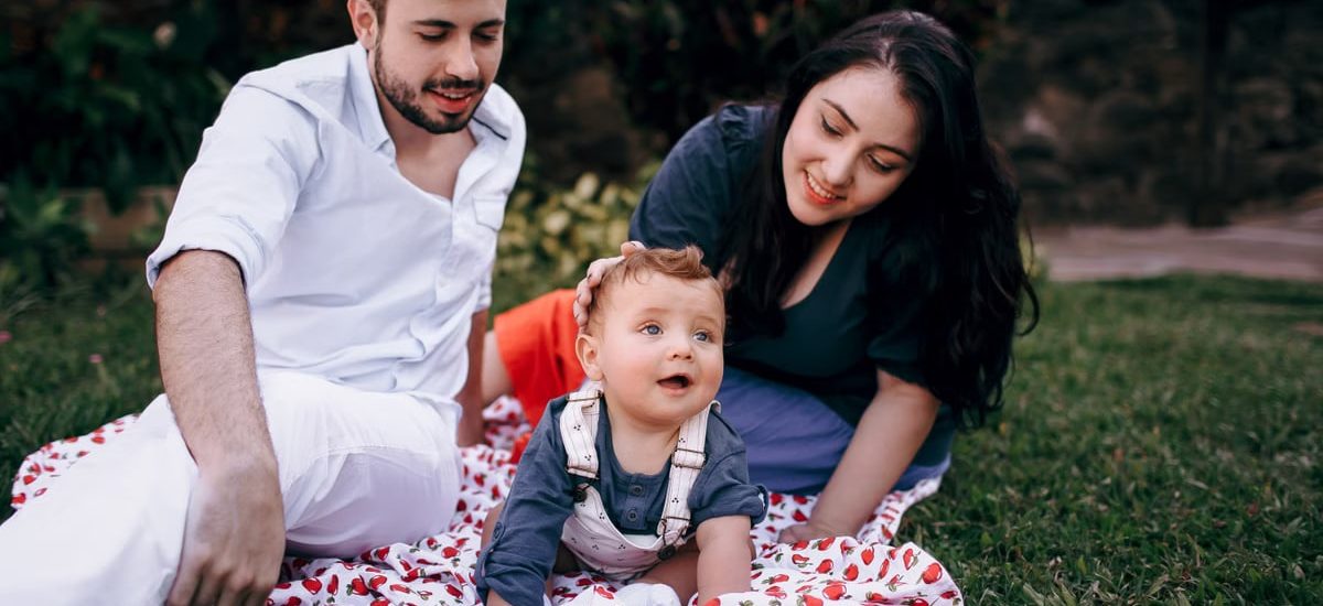 A joyful family enjoying a picnic outdoors during summer. Smiling parents with their baby on a blanket.