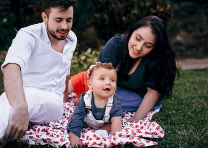 A joyful family enjoying a picnic outdoors during summer. Smiling parents with their baby on a blanket.