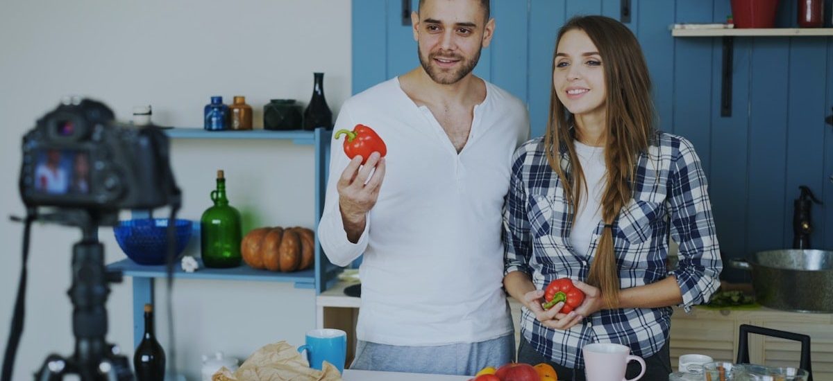 Young attractive couple recording video blog about vegetarian healthy food on dslr camera in the kitchen at home