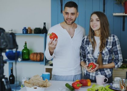 Young attractive couple recording video blog about vegetarian healthy food on dslr camera in the kitchen at home